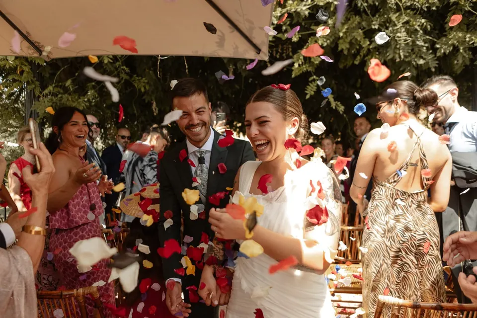 Novios riendo bajo una lluvia de pétalos el día de su boda